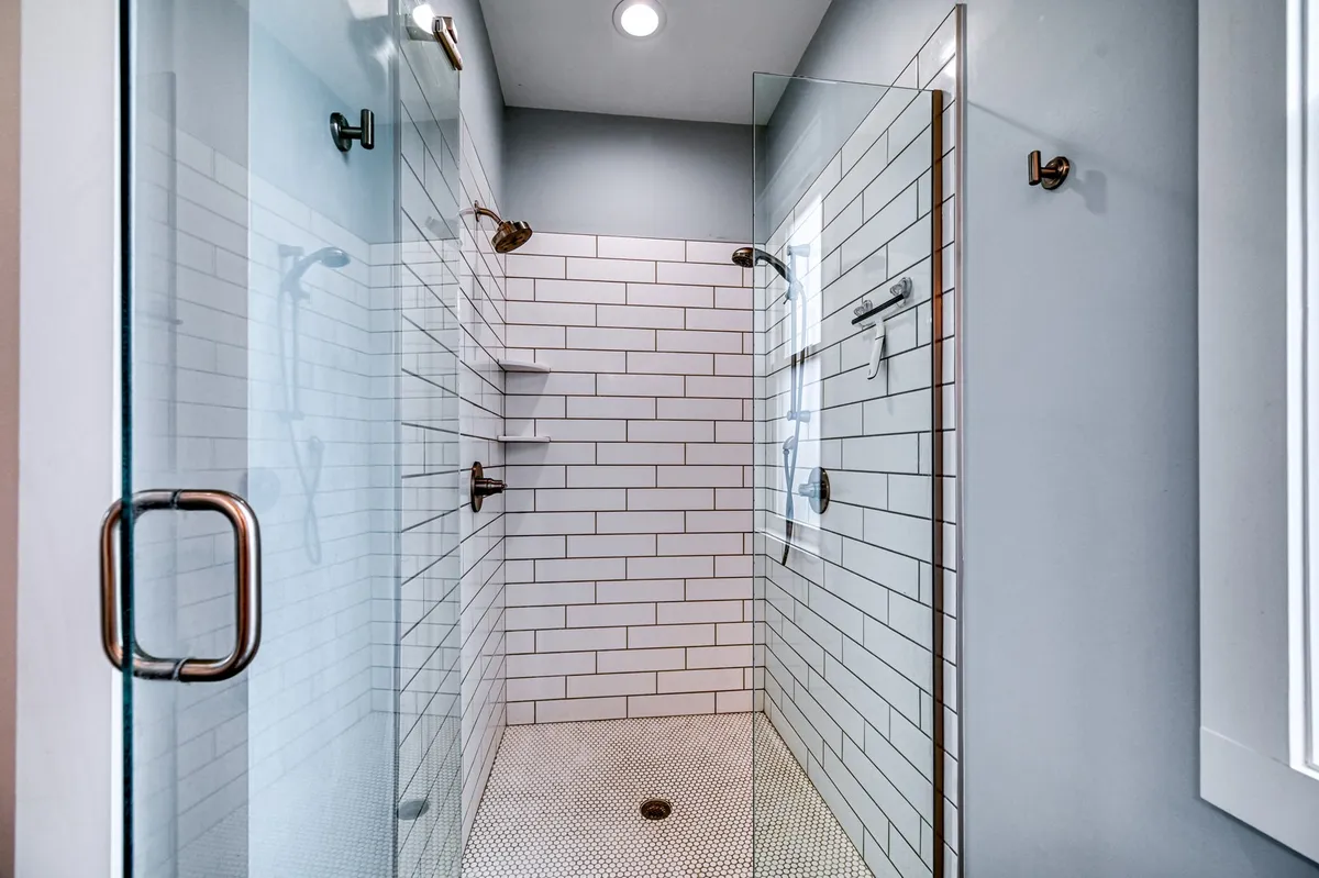 A modern bathroom with a frameless glass shower enclosure, gleaming white subway tiles, and bronze fixtures. The shower offers dual heads and an inviting, spa-like ambiance for invigorating showers or quiet relaxation.
