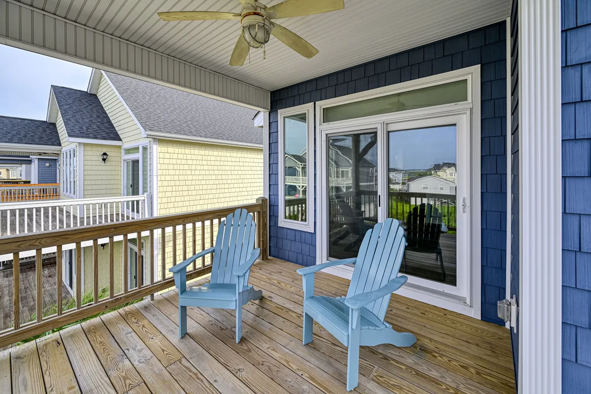 A tranquil outdoor deck scene with blue Adirondack chairs facing an inviting view, a glass sliding door behind, and wooden decking underfoot. The atmosphere is relaxed, suggesting a perfect spot for guests and pets to unwind together after a day of adventures.