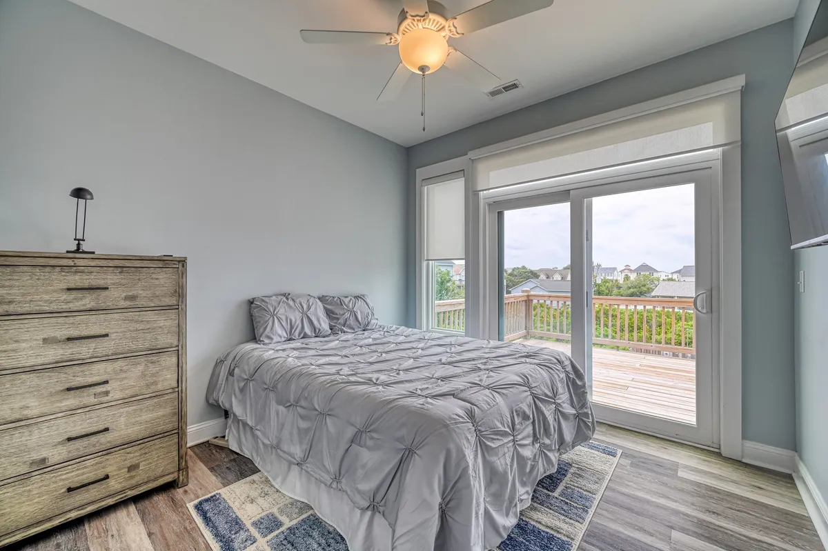 A peaceful bedroom setup with a plush bed, a dresser, and sliding glass doors that open to a scenic view outside. The room exudes a restful vibe, perfect for cozy evenings and private relaxation after a day spent exploring the town or beach.