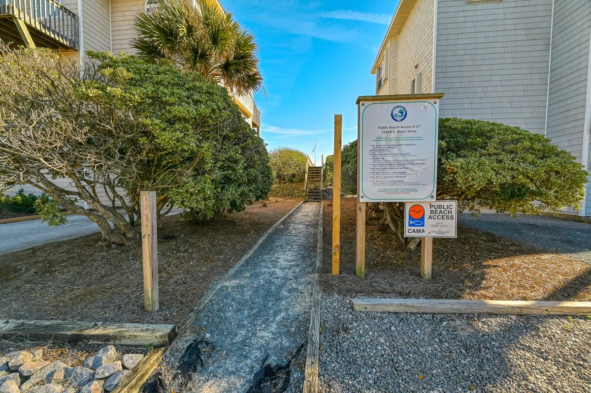 A view of a sandy, inviting pathway lined with greenery, leading directly to the beach. A public access sign marks the route, underscoring the convenience and accessibility for families heading out for a day by the ocean. The scene is relaxed, with the promise of sunbathing and playful family outings just steps away.