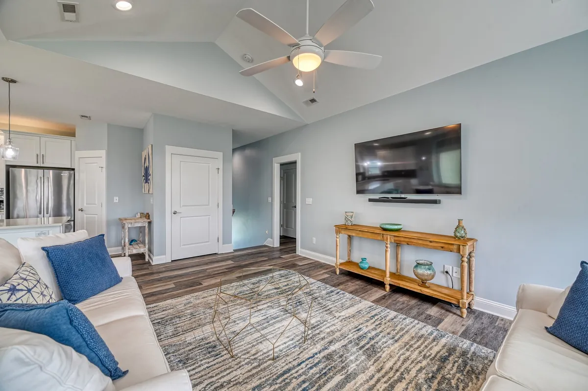 A cozy living room featuring a sofa with blue cushions, a coffee table, and a wall-mounted TV. Decorative items on the side table enhance the inviting atmosphere, making it an ideal space for movie nights, group conversations, or lively game nights.