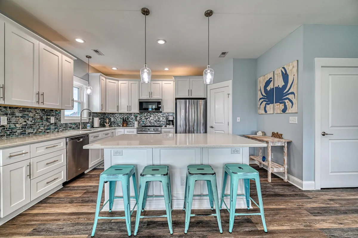 A vibrant kitchen scene featuring a quartz-topped island with turquoise stools, stainless steel appliances, and cheerful blue crab artwork. The space is set up for social cooking, entertaining, and group meals, capturing the essence of shared mealtimes.