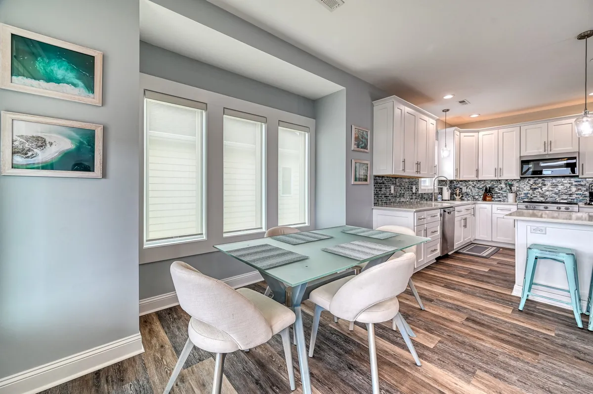 A dining area with a spacious table, surrounded by large windows that fill the room with sunlight. The kitchen cabinetry and decorative art create a warm, inviting space for family meals and casual gatherings, seamlessly connecting to the kitchen and living areas.