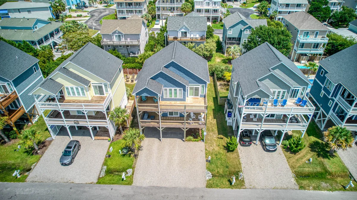 A cheerful exterior view of colorful beach houses with gravel driveways and lush greenery, capturing the laid-back, community vibe of the neighborhood. The scene hints at a safe and low-traffic environment, perfect for exploring with pets.